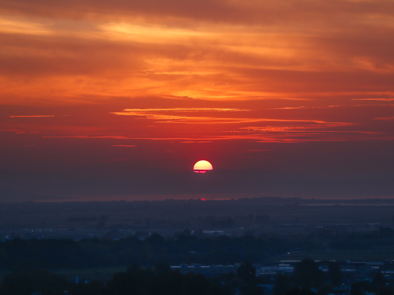 the sun begins to set lighting the sky red and somehow throwing the town and trees in blue shadow